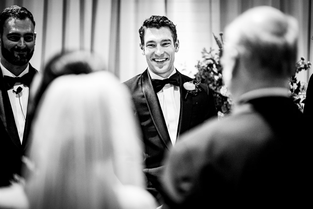 Groom sees bride for the first time in her wedding dress as she walking down the aisle with her dad..